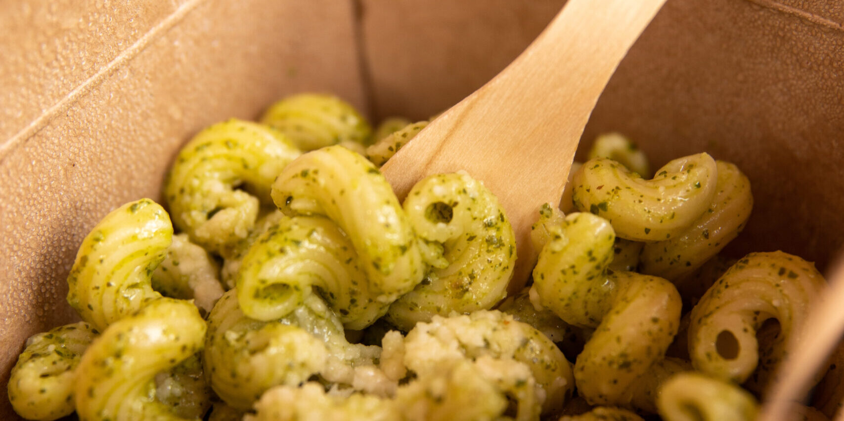 Pesto pasta is served in a compostable container with a compostable wooden fork.